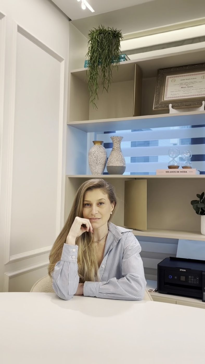 Dra. Michelle Giovanella sentada no consultório, de camisa azul clara